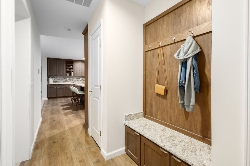 Hallway with a wooden bench, hooks, and cabinets; a jacket and purse hang.
