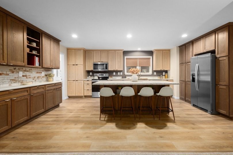 Modern kitchen with wood cabinets, island, stainless steel refrigerator, and white countertops.