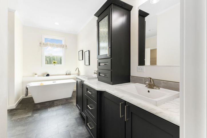 Bathroom with dark cabinets, white countertop, freestanding tub, and window.