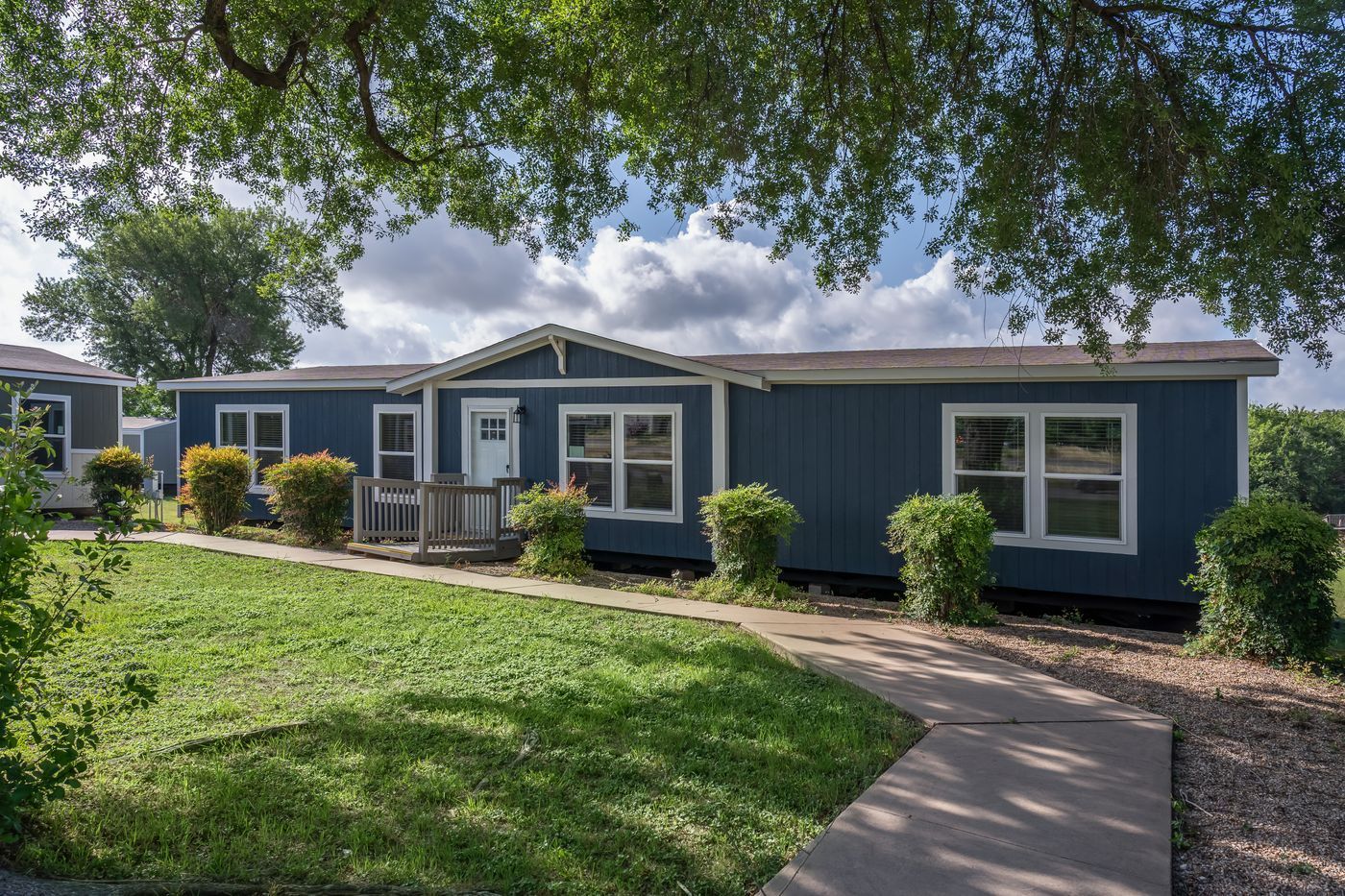 Blue house with white trim, green lawn, trees, and a walkway.