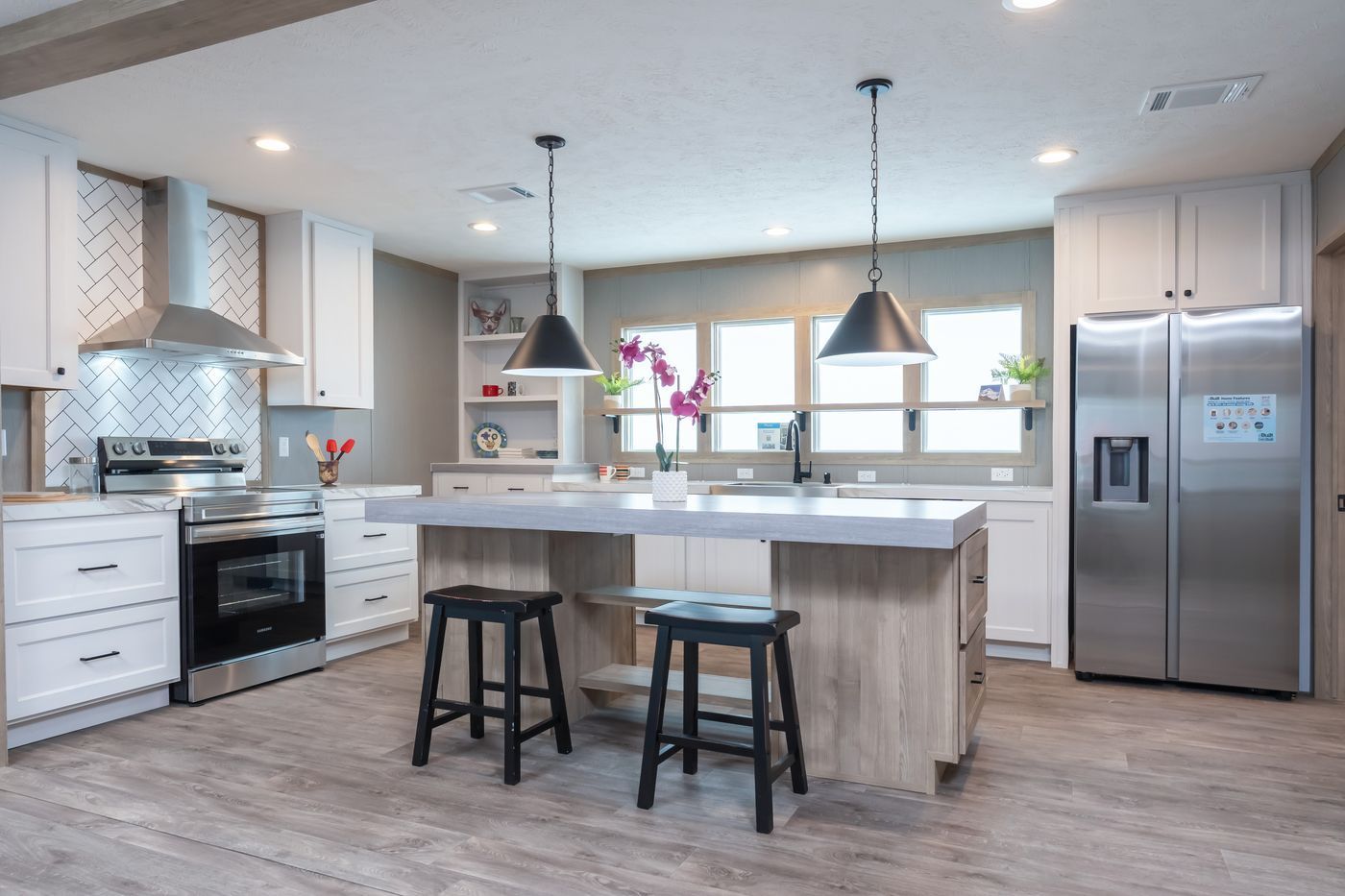 Modern kitchen with white cabinets, stainless steel appliances, island, and two black pendant lights.