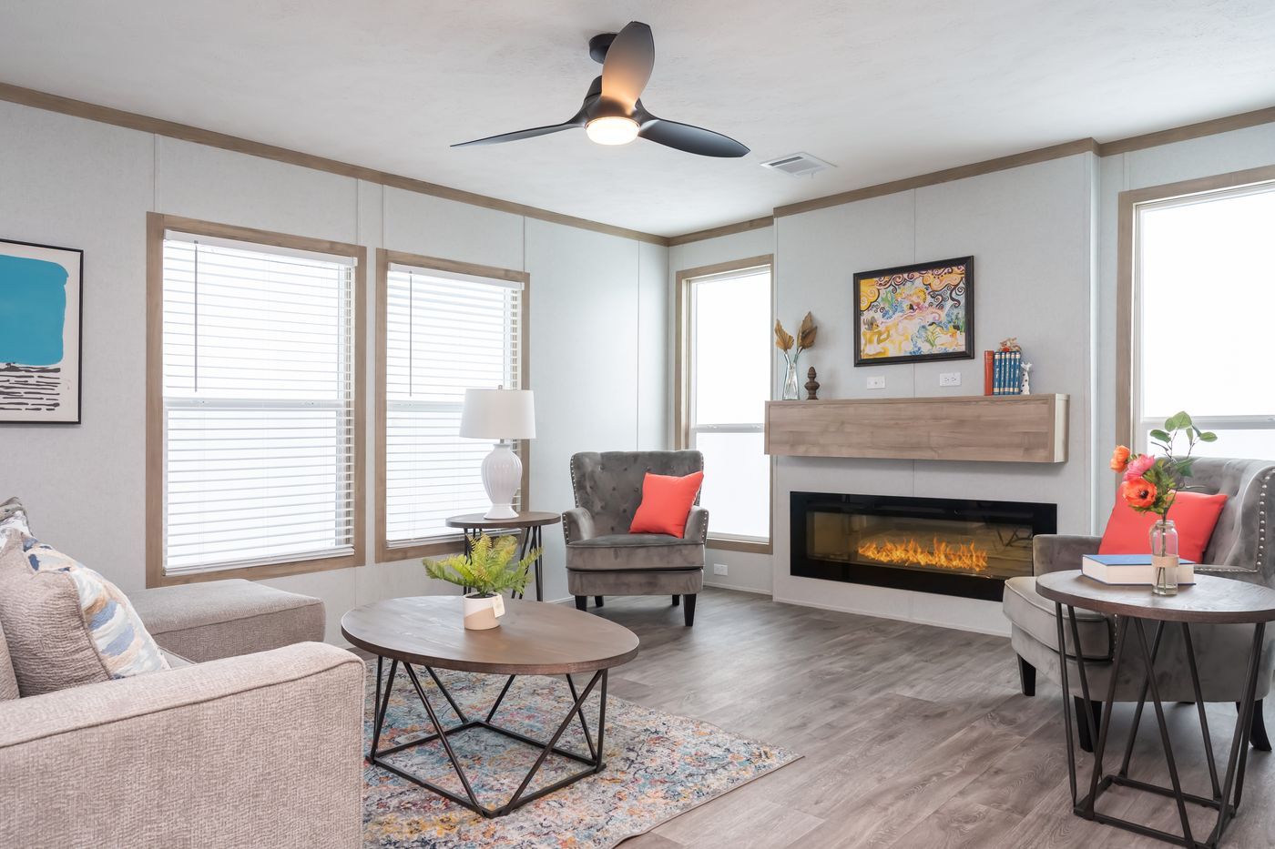 Living room with sofa, chairs, fireplace, and fan; light gray walls, wooden trim, and windows.