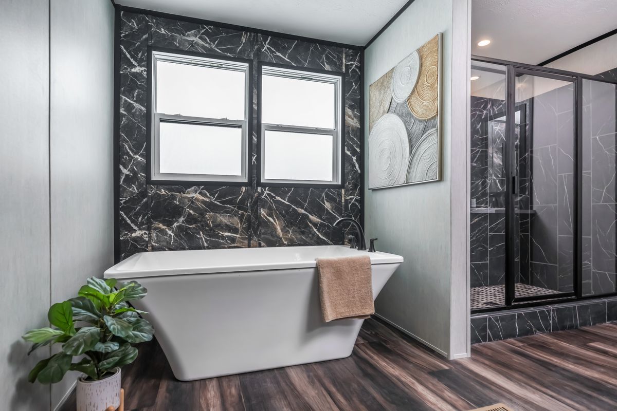 Bathroom with black marble accent wall, white tub, windows, and glass shower.