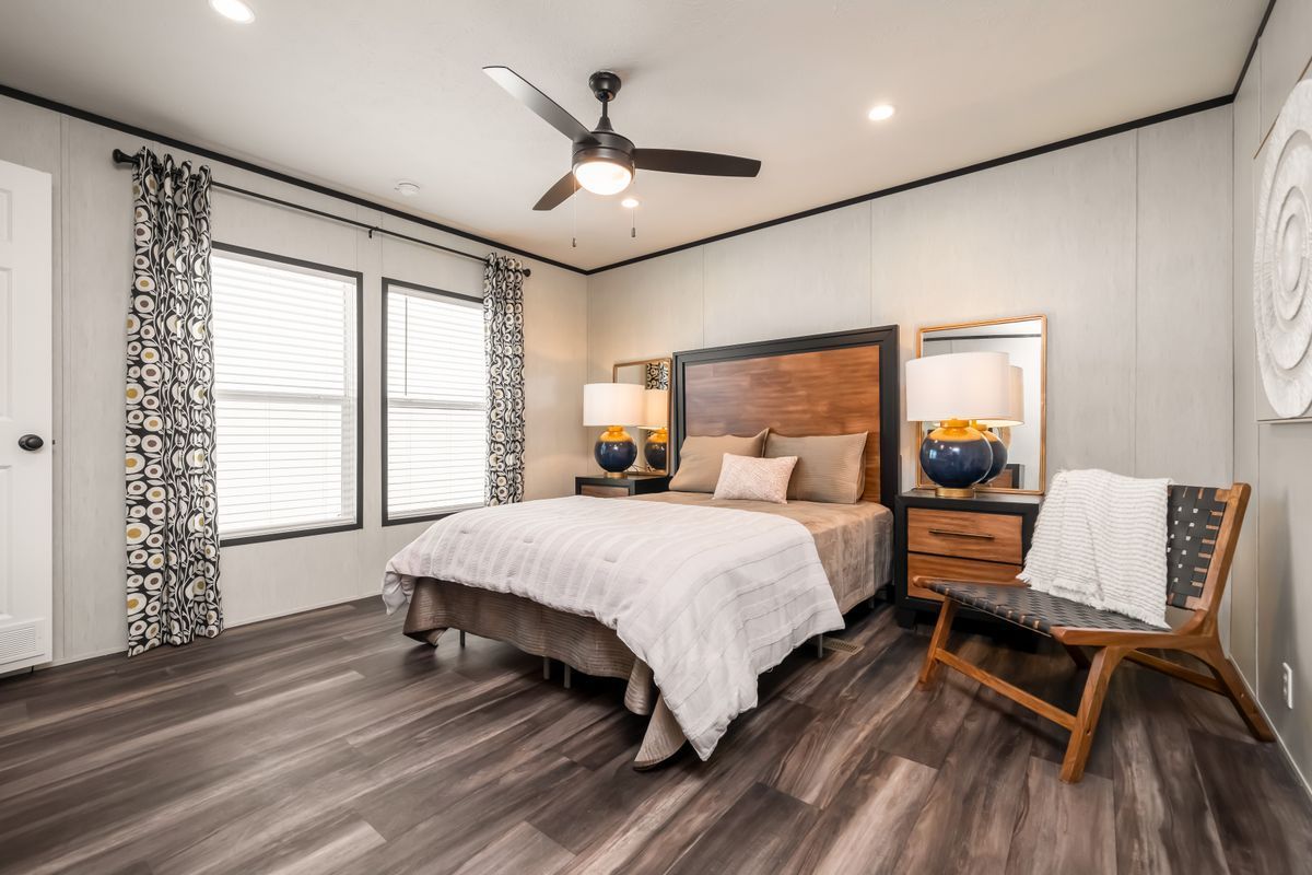 Bedroom with dark wood bed, accent chair, and large windows with blinds.