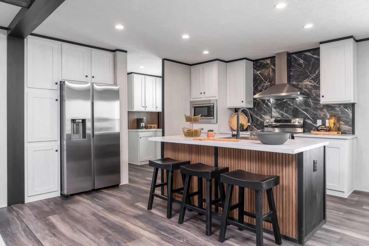 Modern kitchen with white cabinets, stainless steel appliances, island with stools, and wood-look flooring.