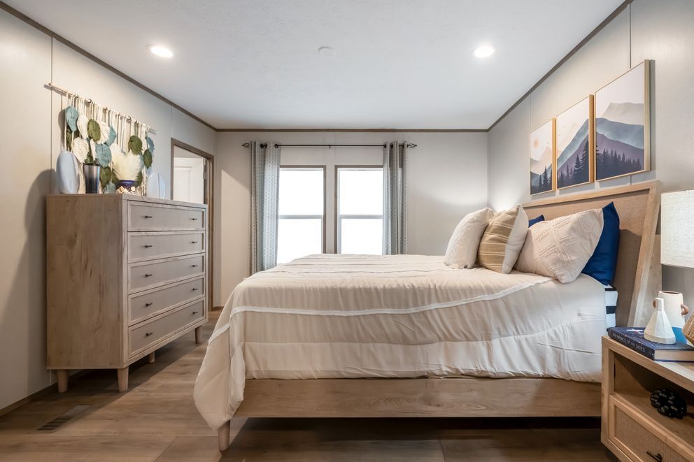 Bedroom with light wood furniture, white bedding, and framed mountain art.