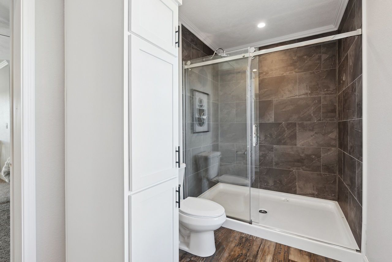 Bathroom with a white cabinet, a toilet, and a glass-enclosed shower with brown tile walls.