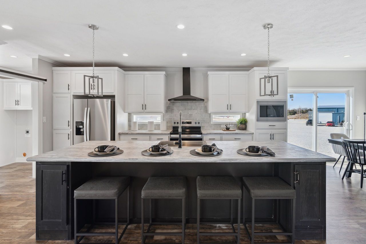 Modern kitchen with a large island, white cabinets, stainless steel appliances, and gray stools.
