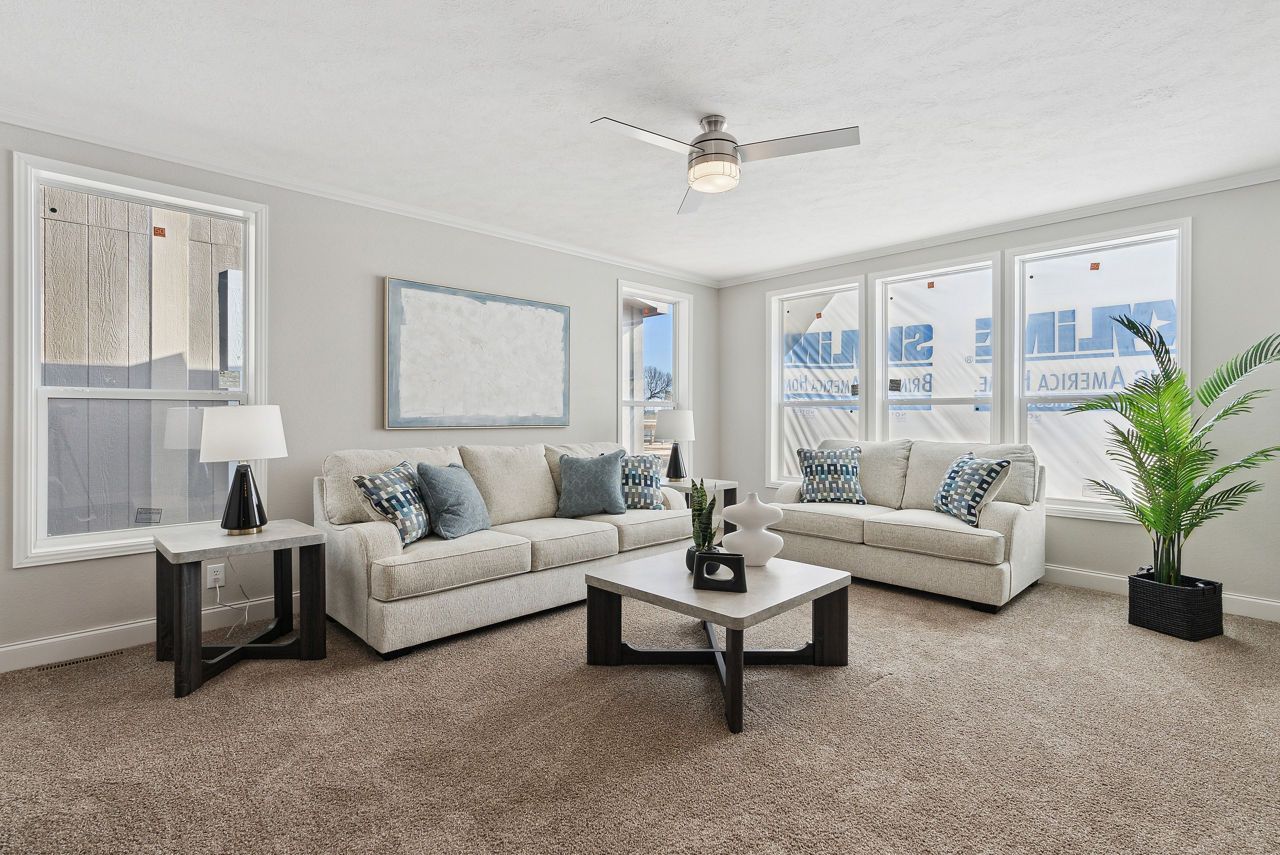 Living room with couches, coffee table, and large windows. Beige carpet and gray walls.