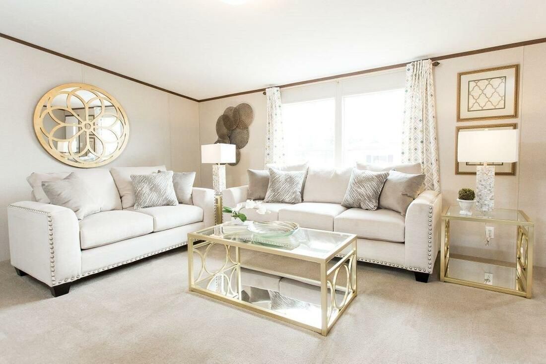 Living room with white sofas, gold accents, glass coffee table, and large window.