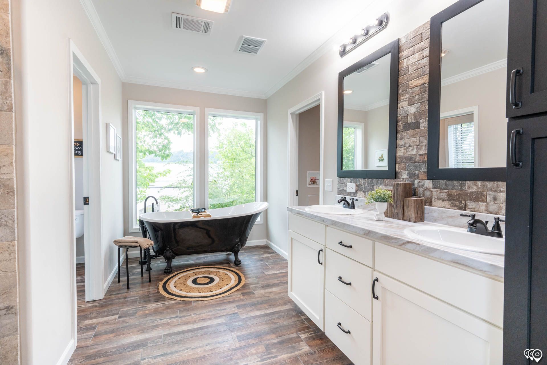 Bathroom with freestanding black bathtub by a window, double vanity, and dark accents.