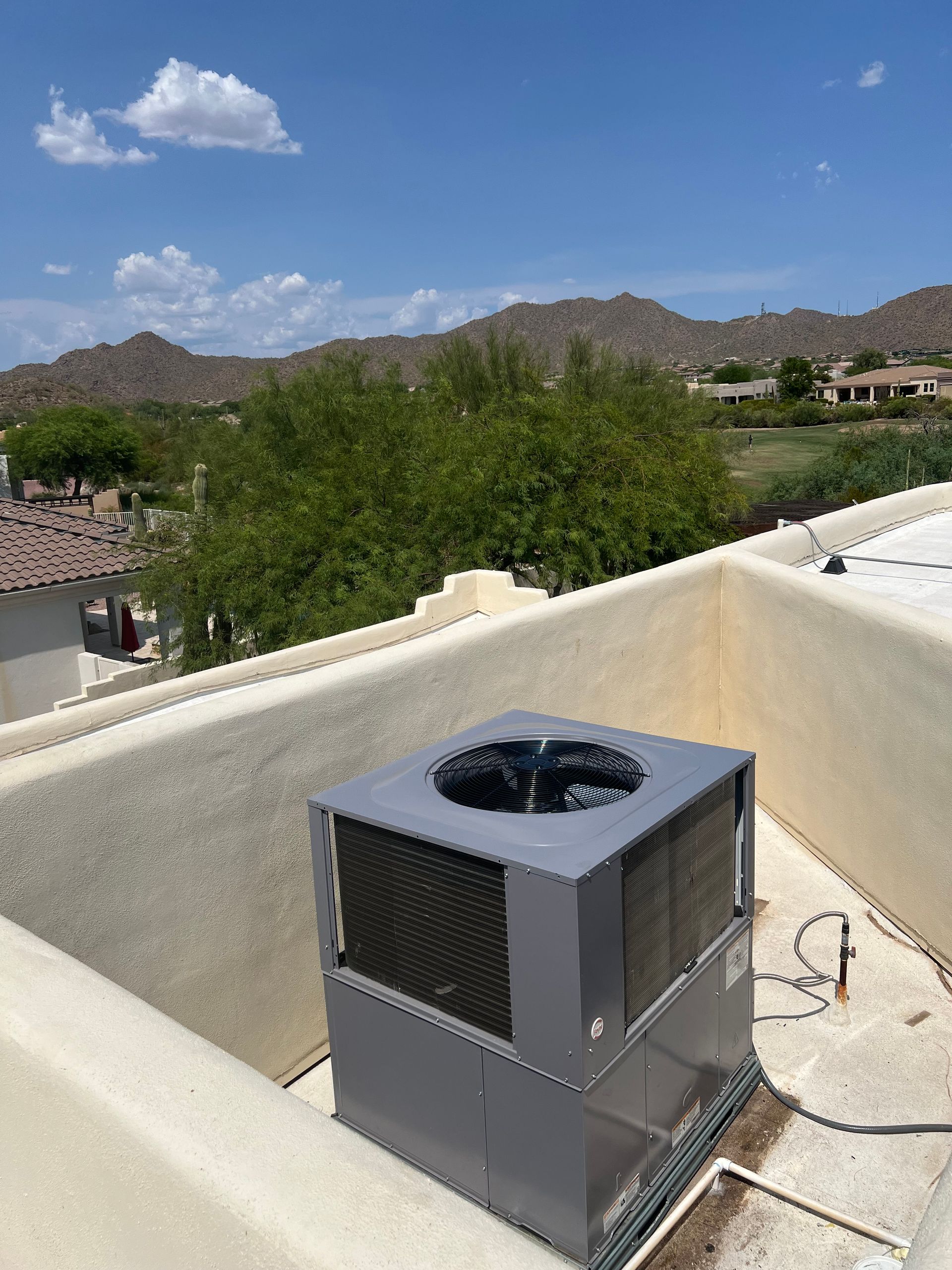 An air conditioner is sitting on top of a roof with mountains in the background.