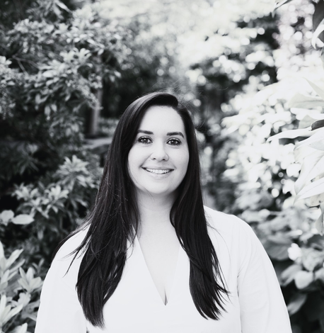Woman in blazer smiles, posed in a bright office, wearing jewelry.