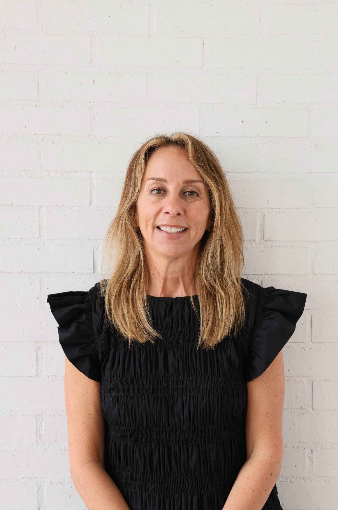 A woman in a black dress is standing in front of a white brick wall.