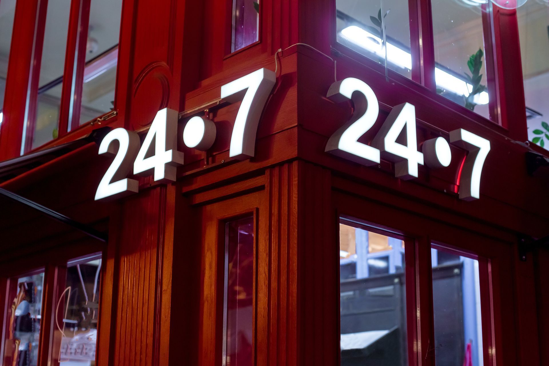 A brightly illuminated 24/7 sign glowing on a red storefront corner.