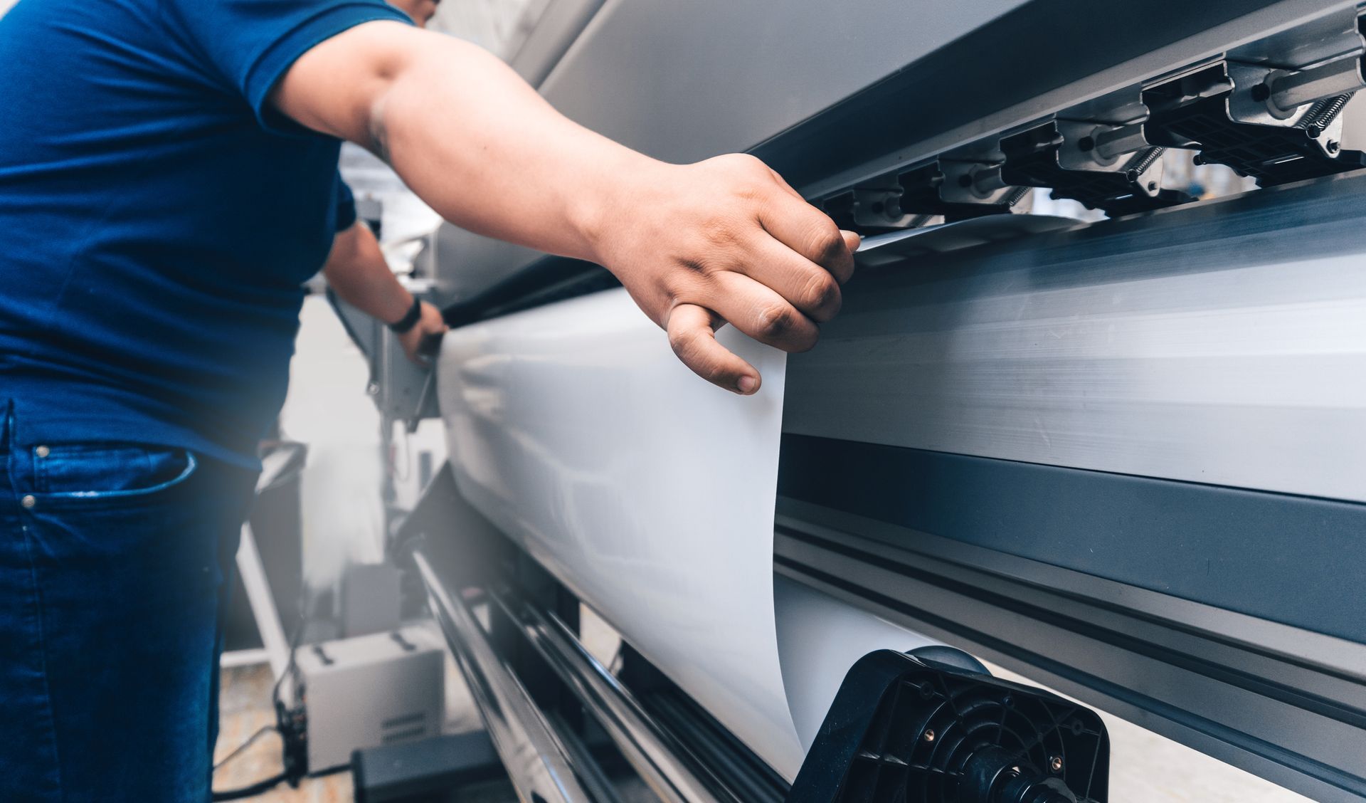 Man holds sheet to a printing plotter, showing the sign manufacturing services Cardinal Sign Corporation has in Hampton, VA.