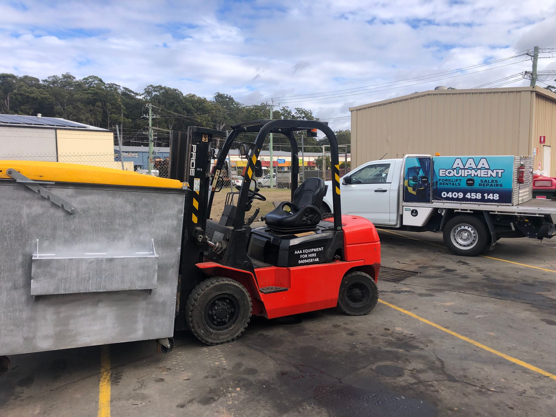 Red forklift lifting a dumpster in a yard— AAA Equipment Pty Ltd In Port Macquarie, NSW