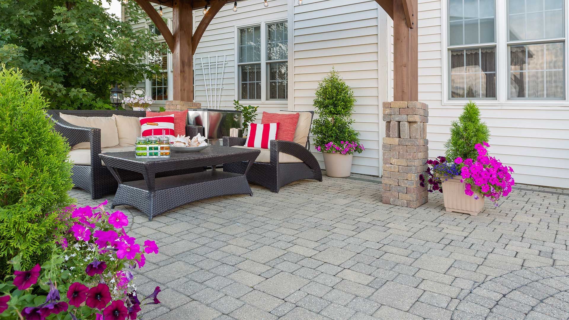 A patio with a gazebo , couch , table , chairs and purple flowers.