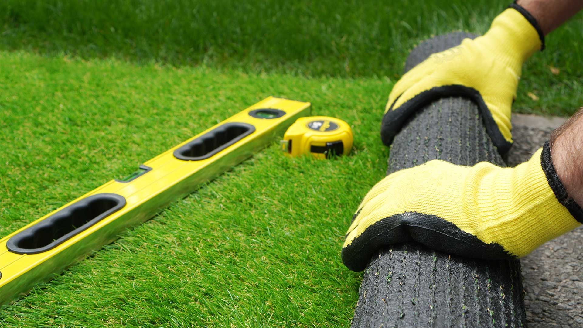 A person is measuring a piece of grass with a tape measure and a level.