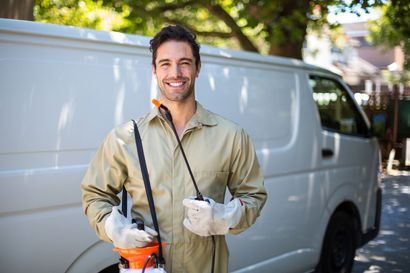 Smiling pest control technician with sprayer, standing by a white van.