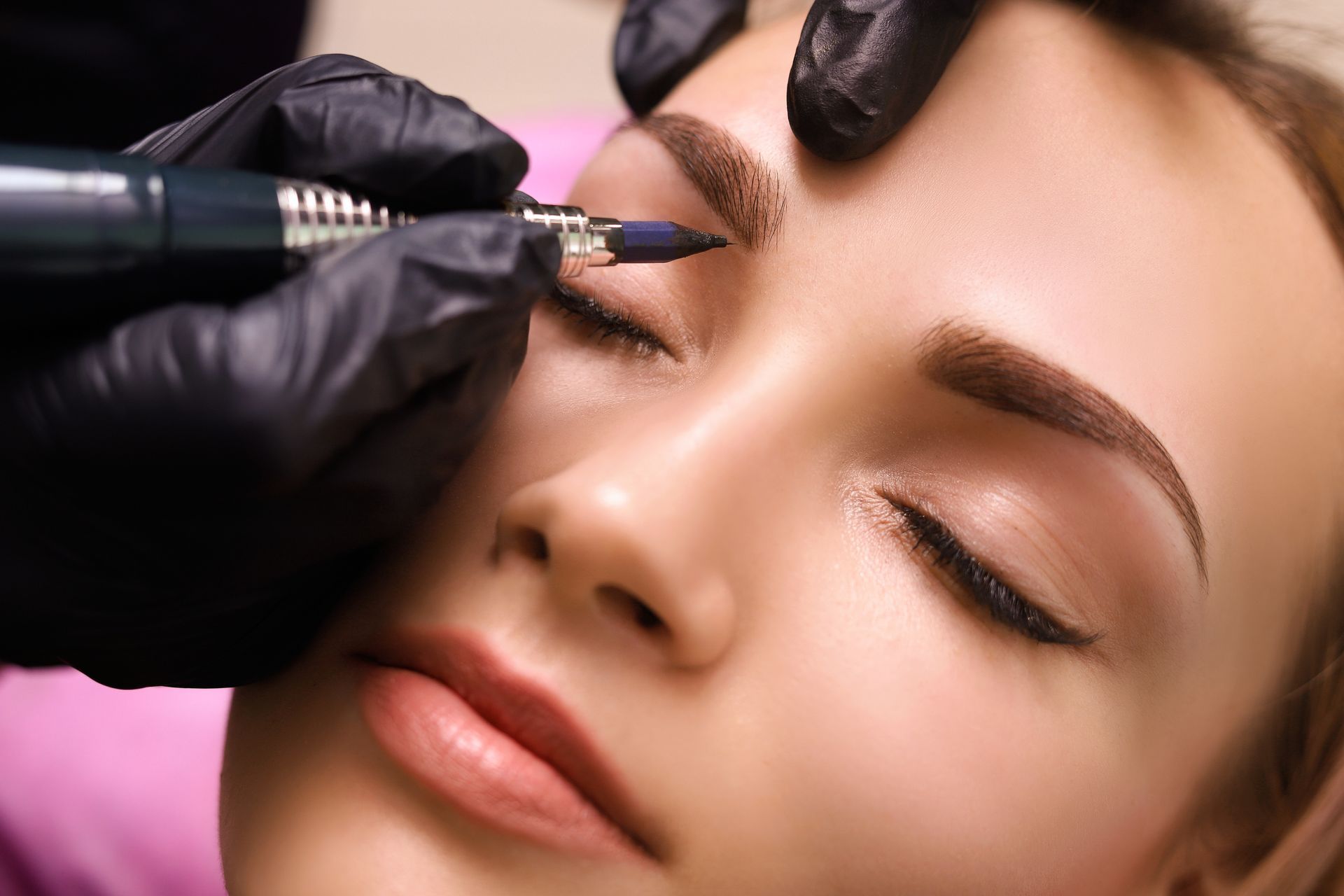 Person, die sich einer kosmetischen Augenbrauenbehandlung unterzieht; Technikerin die einen Tätowierstift benutzt.