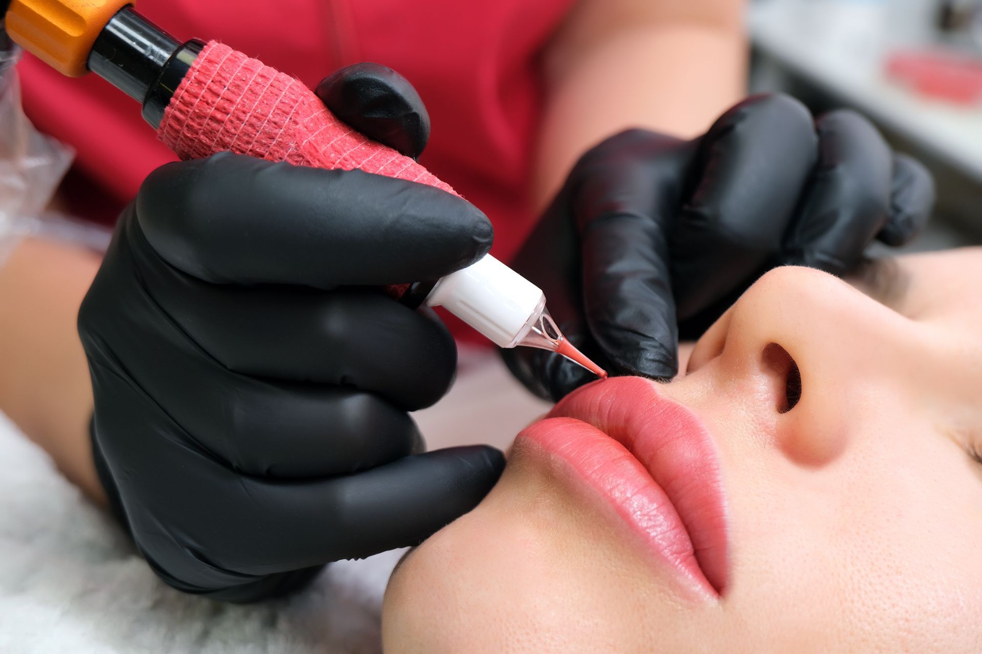 Lippenpigmentierungs-Tattoo-Prozedur an den Lippen einer Person. Hände in schwarzen Handschuhen halten das Gerät.