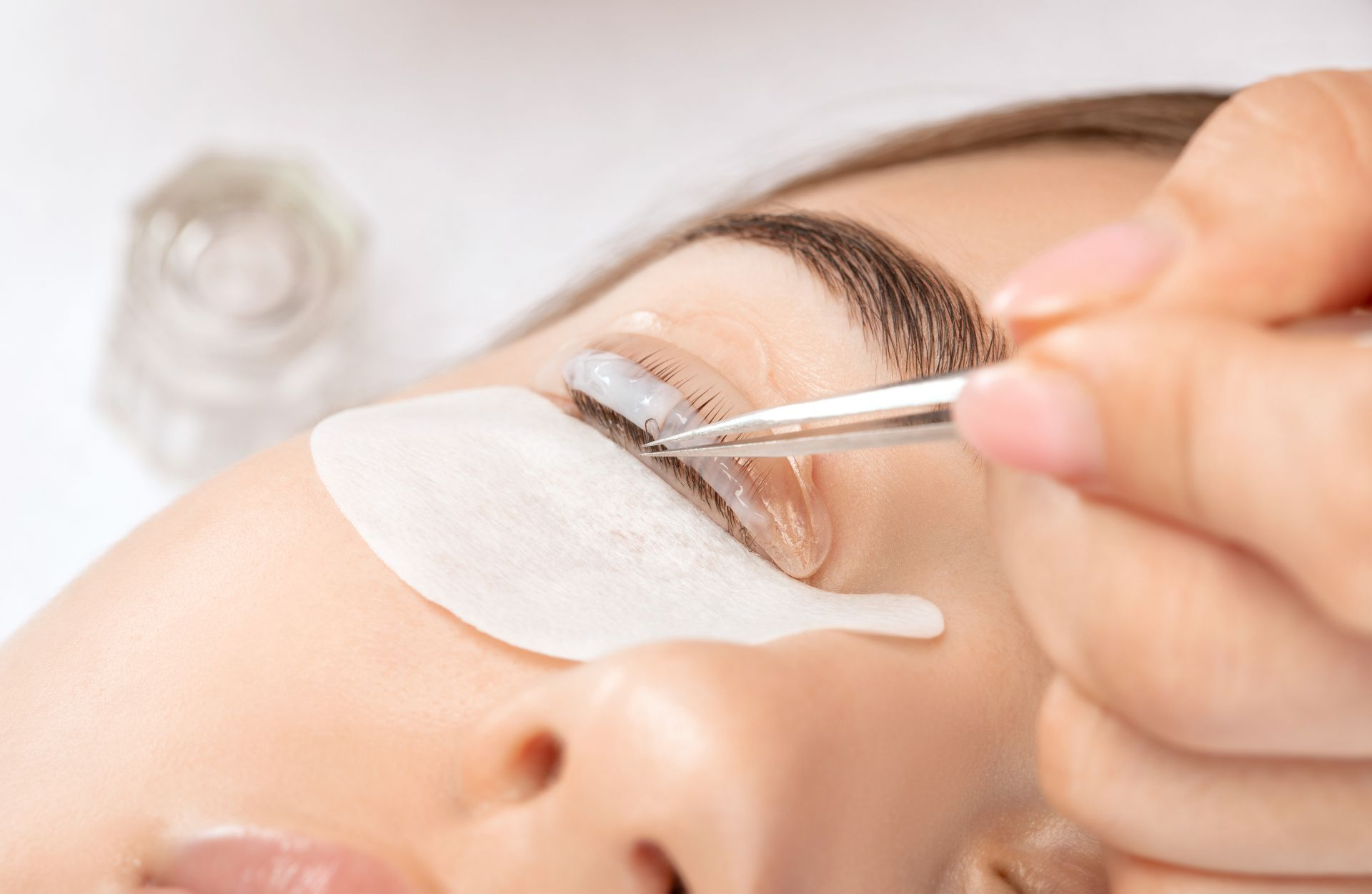 Eine Person unterzieht sich einer Wimpernlifting-Behandlung. Eine Kosmetikerin trägt eine Creme auf die Wimpern auf.