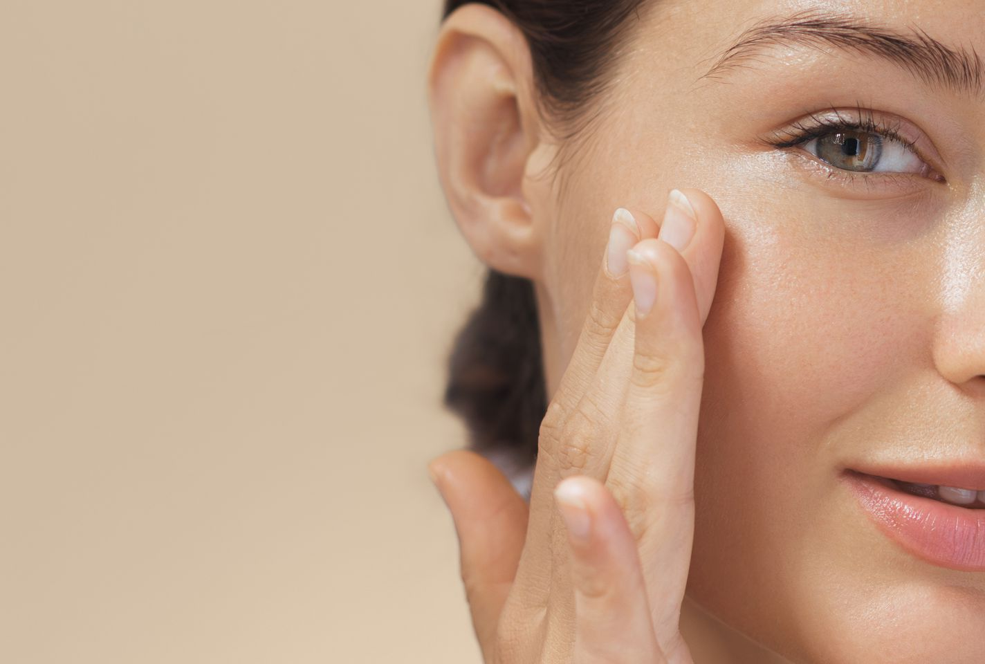 Frauenhand berührt sanft die Wange; helle Haut, neutraler Hintergrund, lächelnd.