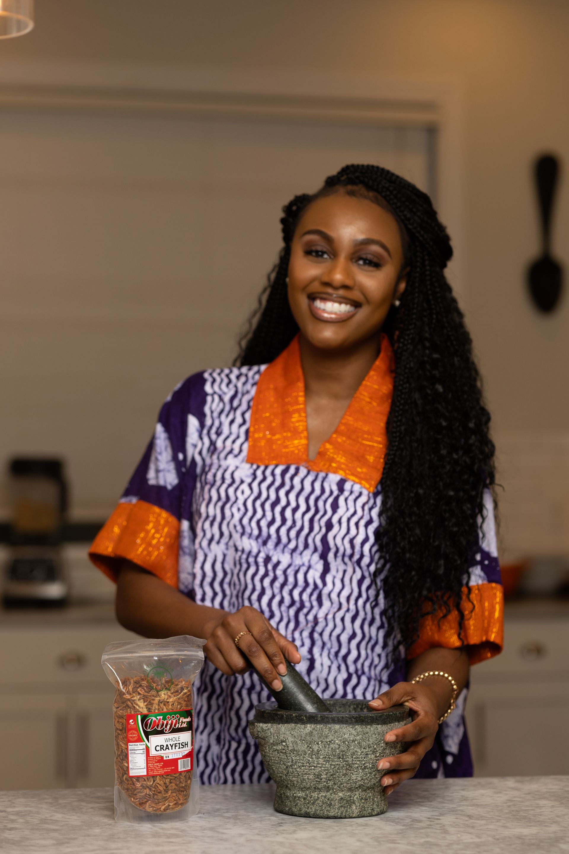 A woman is standing in a kitchen holding a mortar and pestle.