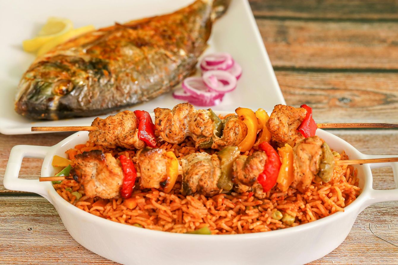 A bowl of rice and skewers with a fish on a plate in the background.