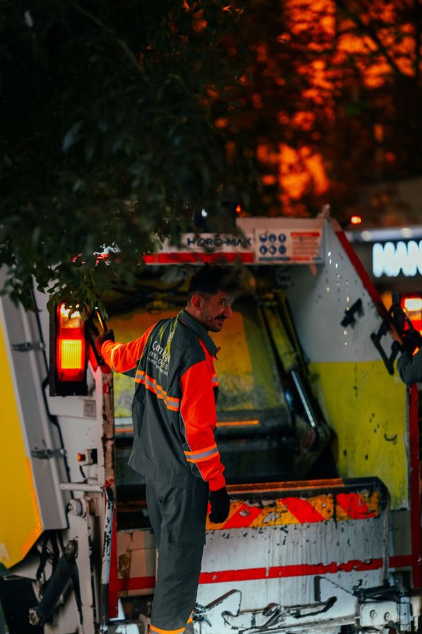 Person in reflective workwear standing beside a truck under tree branches at night