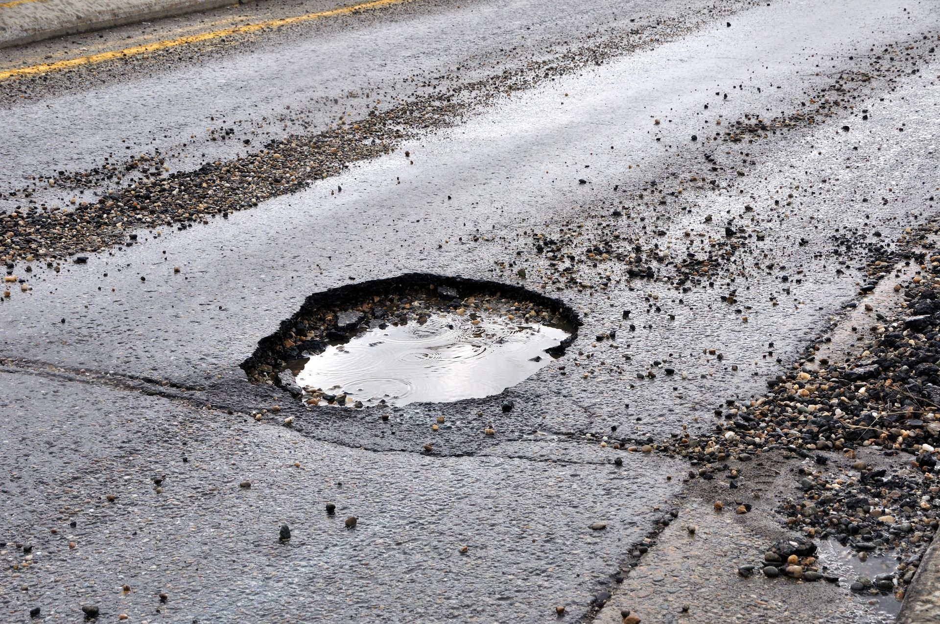A water-filled pothole on a worn asphalt road surface.