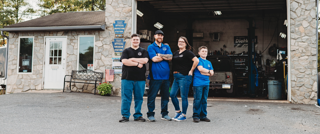 Four people standing in front of a stone building with an open garage. They are wearing blue jeans and work shirts | City Side Auto