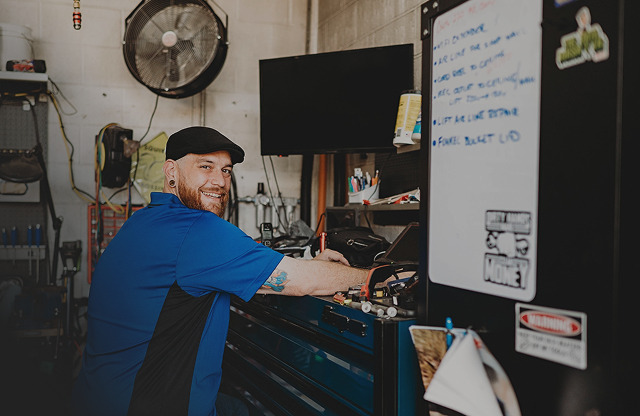 Mechanic in blue shirt, black cap, smiles while working on a toolbox in a shop | City Side Auto