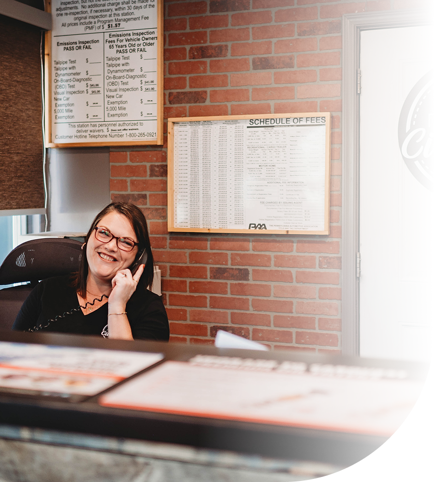 Woman smiling while on the phone at a reception desk. Behind her is a brick wall with charts | City Side Auto