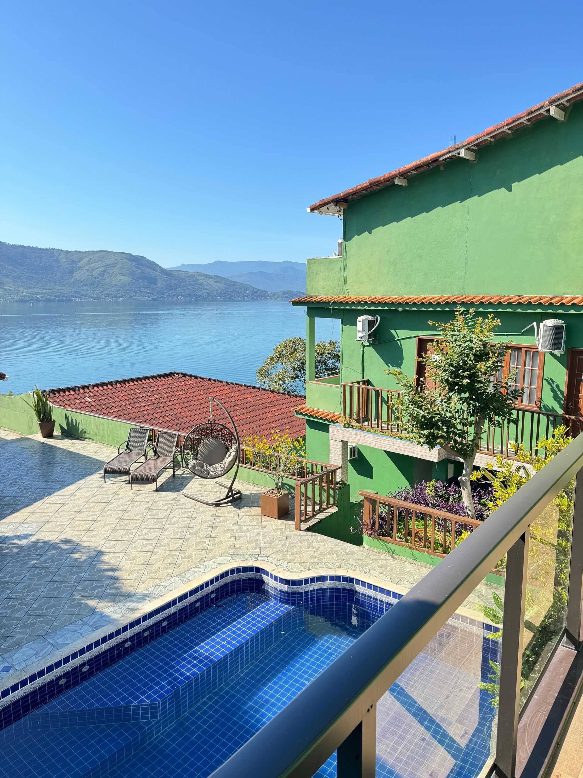 Prédio verde com telhado vermelho com vista para a piscina e o lago.