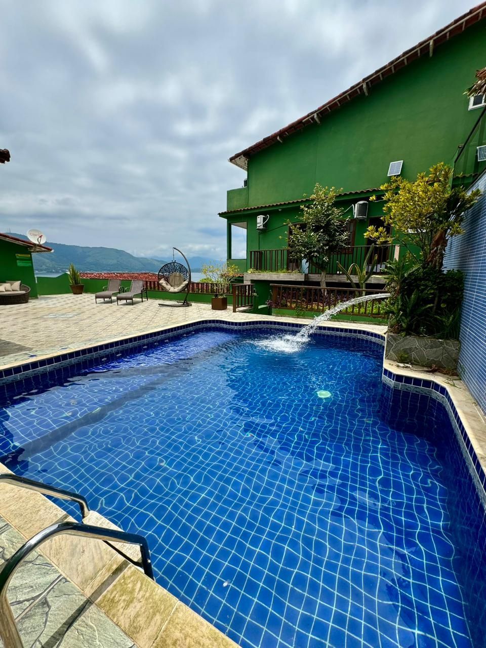Piscina com vista panorâmica e um edifício verde ao fundo.