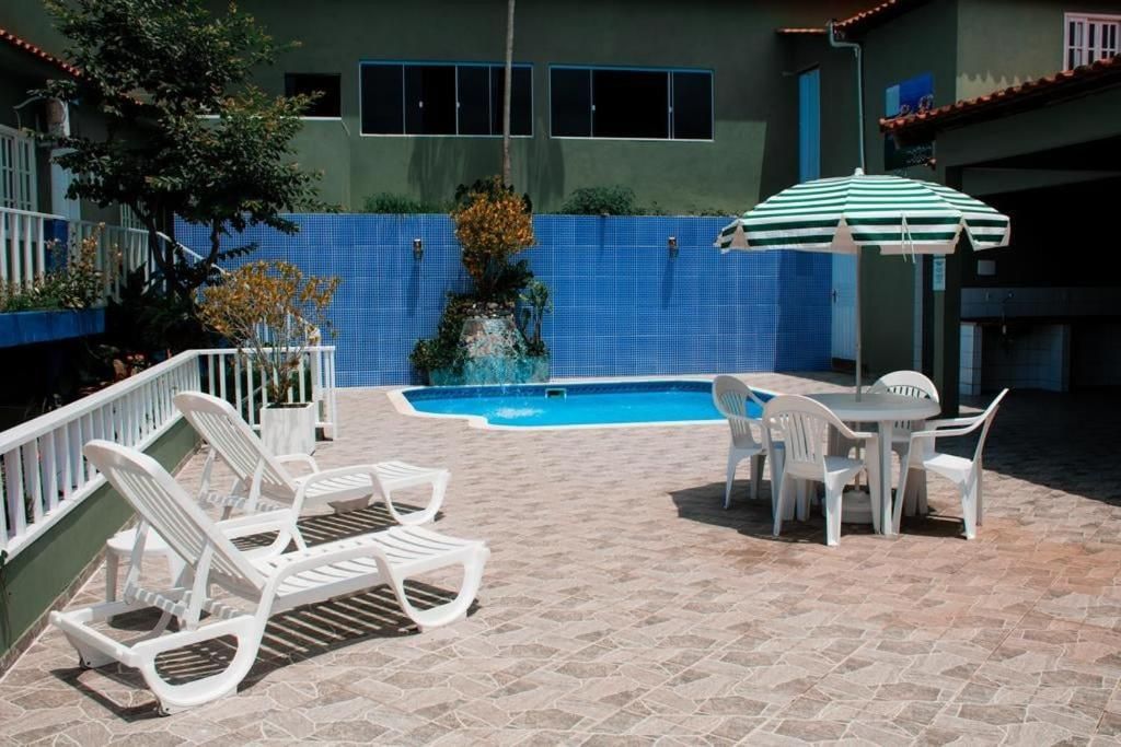 Pátio nos fundos com uma pequena piscina, espreguiçadeiras, uma mesa com cadeiras e um guarda-sol.