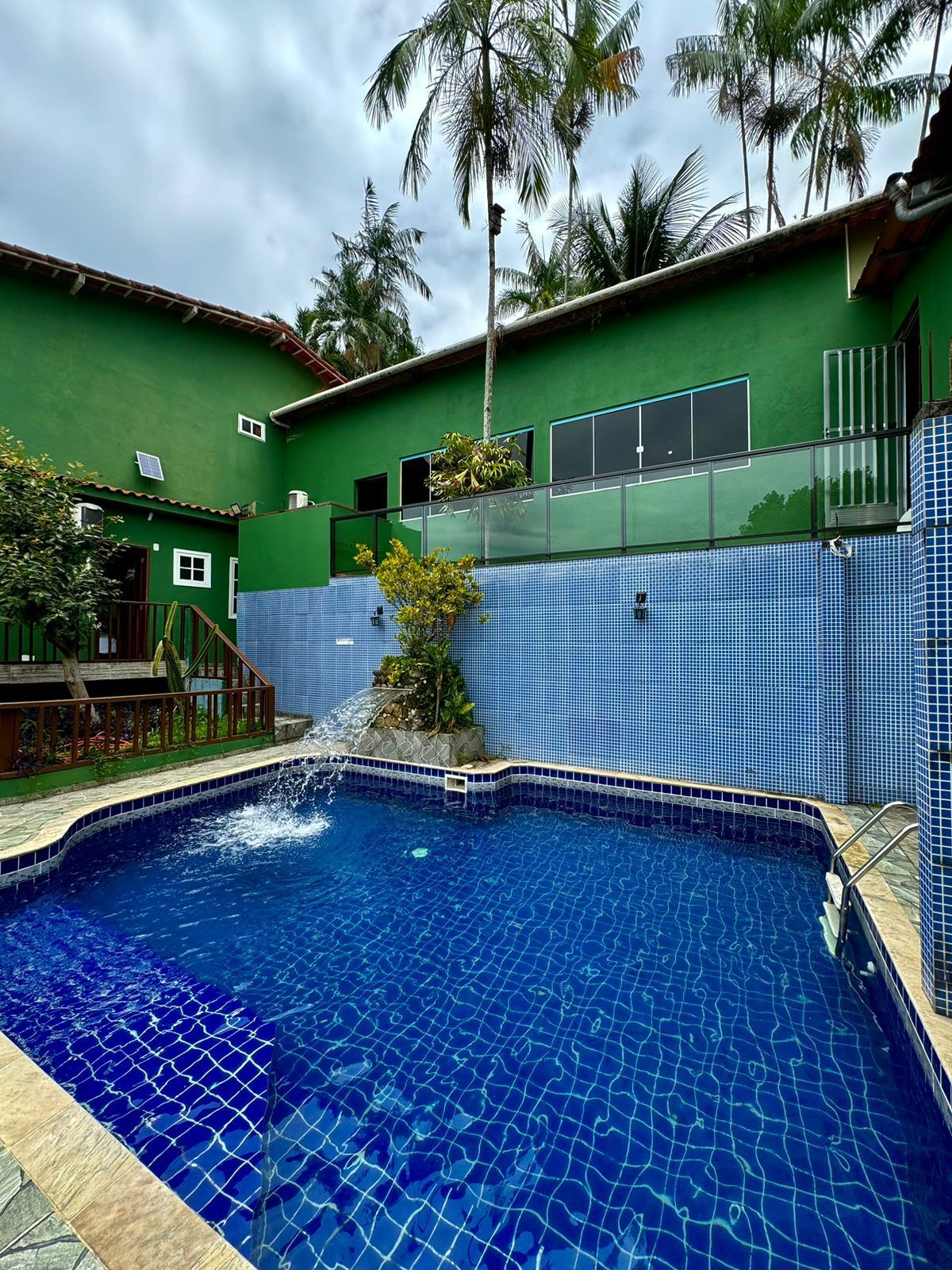 Um quintal com piscina revestida de azulejos azuis, estufa e palmeiras.
