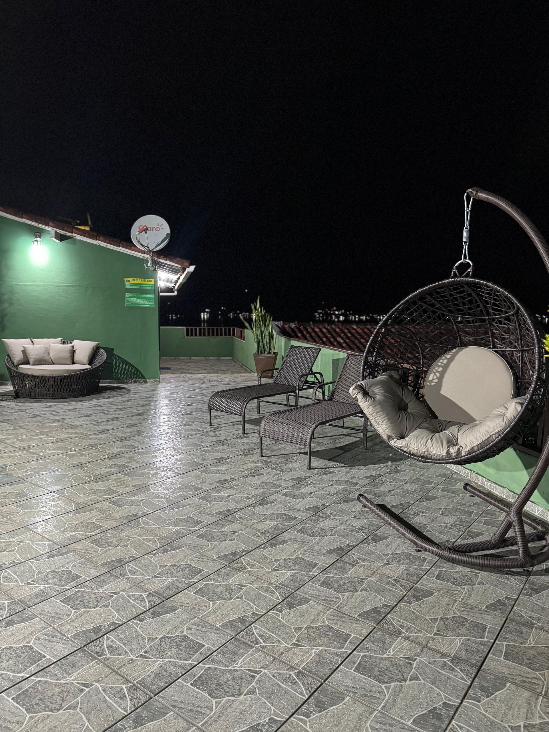 Terraço na cobertura à noite com assentos, incluindo uma cadeira suspensa, um sofá e espreguiçadeiras.