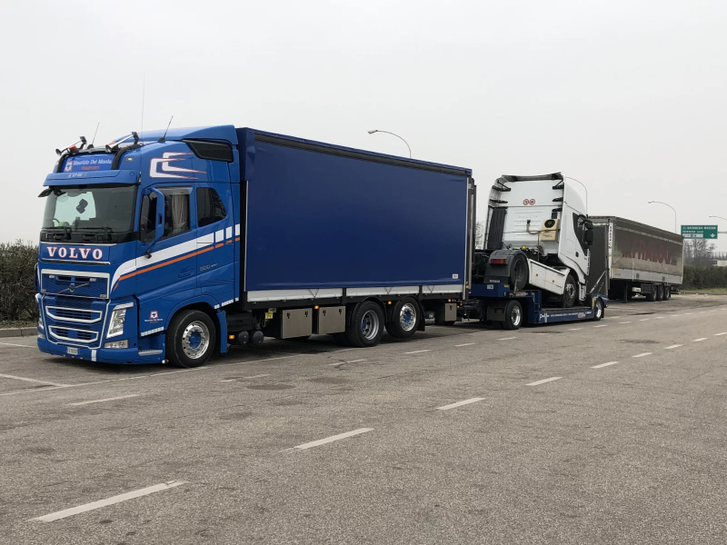 Un semirimorchio Volvo blu in un piazzale, con altri camion e rimorchi parcheggiati alle sue spalle.