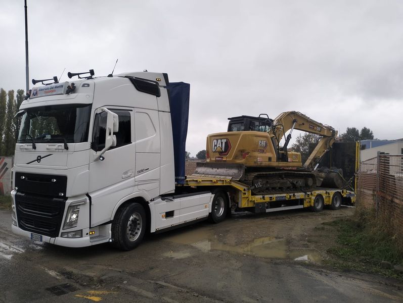 Escavatore rosso caricato su un camion con rimorchio, con la benna sollevata in un cantiere.