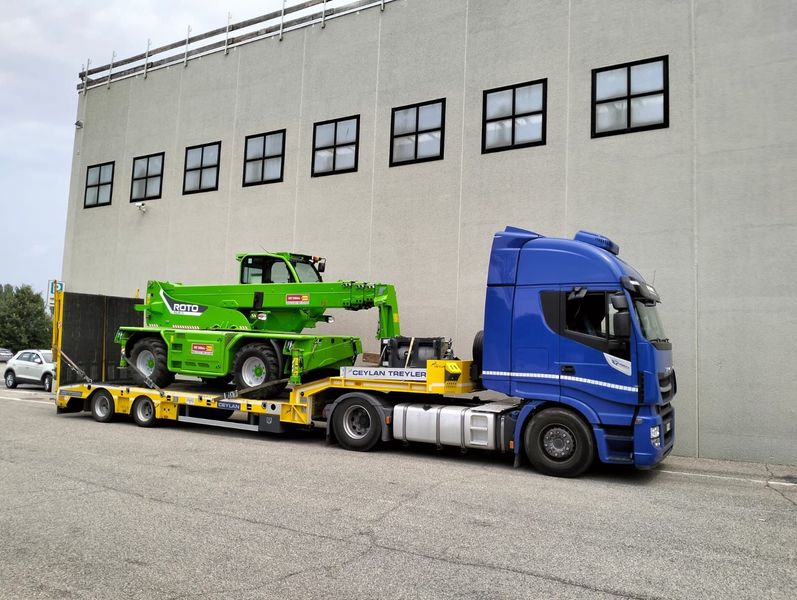 Un semirimorchio blu che trasporta un veicolo da costruzione verde su un rimorchio a pianale giallo