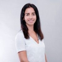 A woman with long dark hair is wearing a white shirt and smiling.