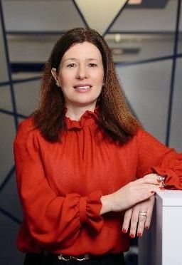A woman in a red blouse is leaning on a counter.