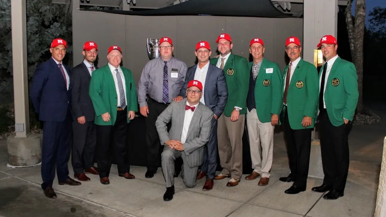 A group of men in suits and green jackets are posing for a picture.