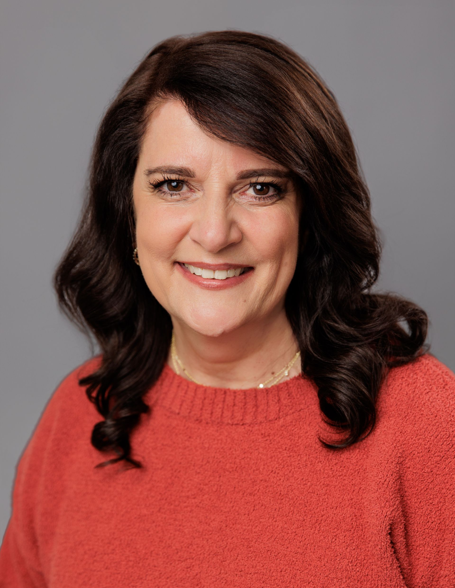 woman smiling at the camera wearing an orange top.