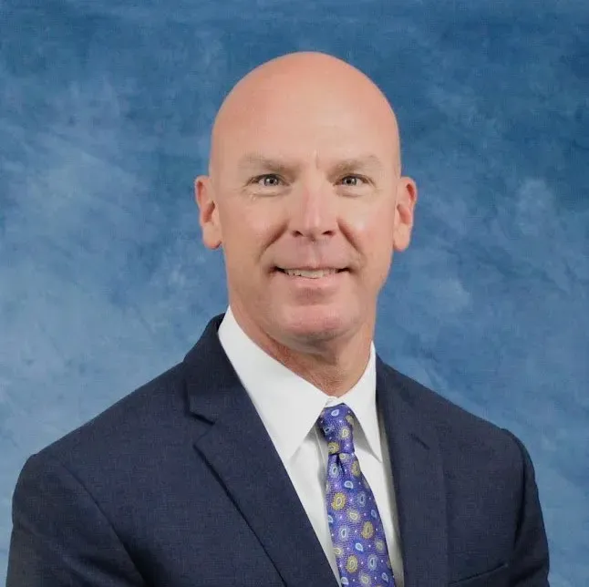 A bald man in a suit and tie smiles for the camera