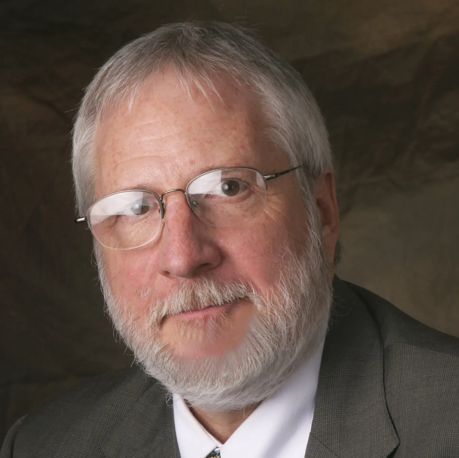 A man with glasses and a beard is wearing a suit and tie