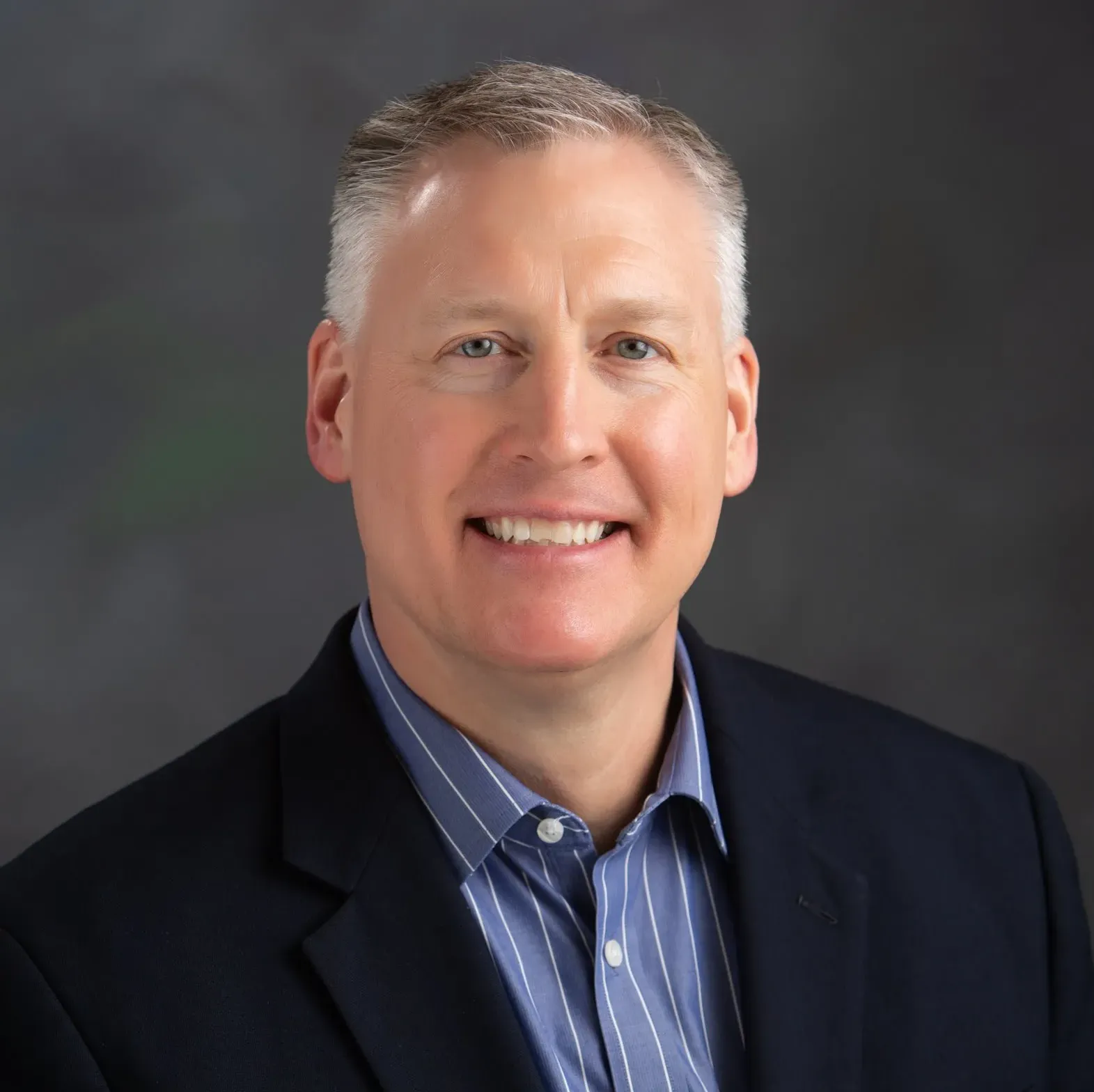 A man in a suit and striped shirt smiles for the camera